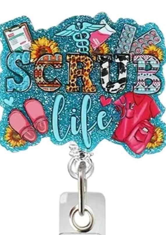 A decorative acrylic badge reel cover featuring the words 'SCRB life' in glittery letters, surrounded by medical-themed illustrations including a stethoscope, clipboard, pink slippers, a red scrub top, and sunflowers. The reel has a silver metal clip and a clear plastic base.